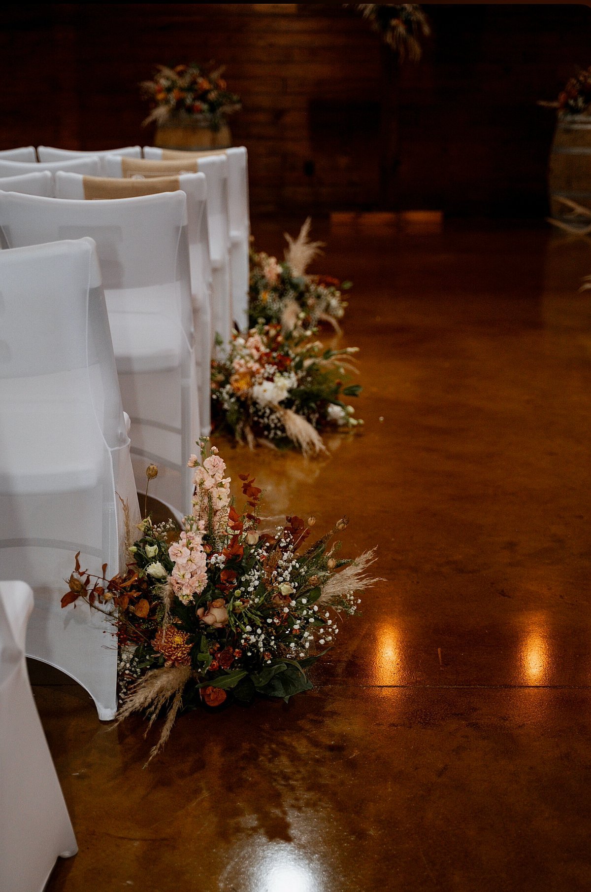 Beautiful wildflower arrangements lining ceremony aisle with white chair covers