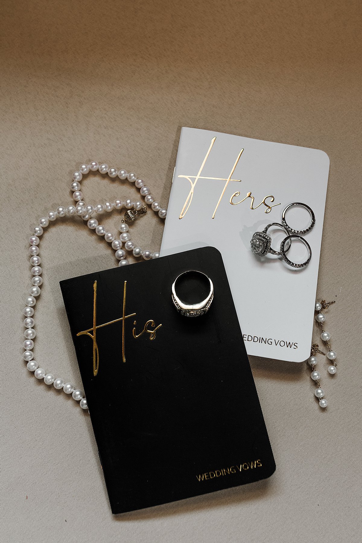 His and Hers wedding vow books with rings and pearl necklace flat lay