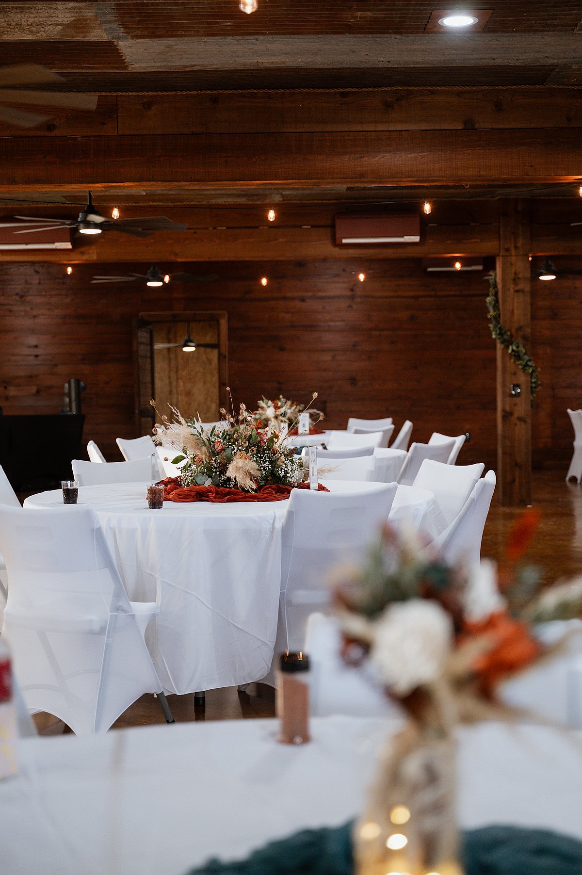 Elegant white table setting with floral centerpieces and string lights in barn